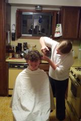 Jocelyn barbering Kevin, who is seated in the kitchen and wrapped in a white sheet