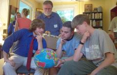 Steve, Mark, and Phil study a globe of the world. Father Gregory looks on.