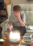 Phil sits before the cake, with his hands covering his face.