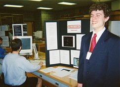 a student is seated using a computer, while Kevin stands beside the display
