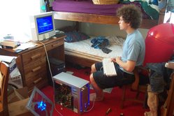 Kevin, seated with keyboard on his lap, next to computer on the floor. The case of the computer is open.