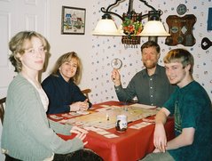 four players around a red kitchen table, with a board game on the table