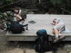 two hikers lieing down on a tent platform, with their packs