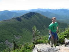 guy in green shirt poses with a rocky summit in background