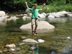 guy perches on a rock in mid-stream, waving both arms