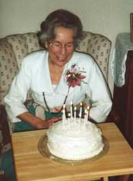 Grandma T seated, with her lighted birthday cake