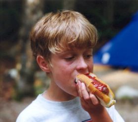 Philip takes a bite out of a ketchup-coated hot dog.